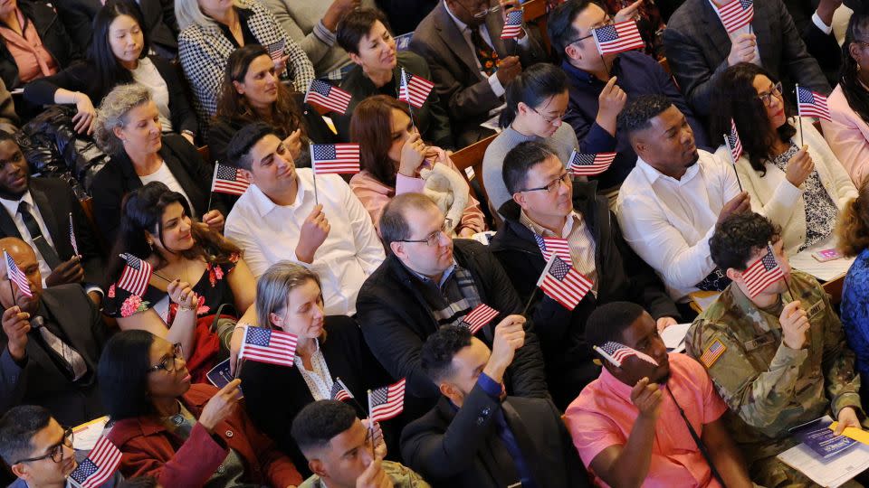 New US citizens wave flags after taking an oath of allegiance during a naturalization ceremony on April 25, 2023, at Faneuil Hall in Boston, Massachusetts. - Brian Snyder/Reuters