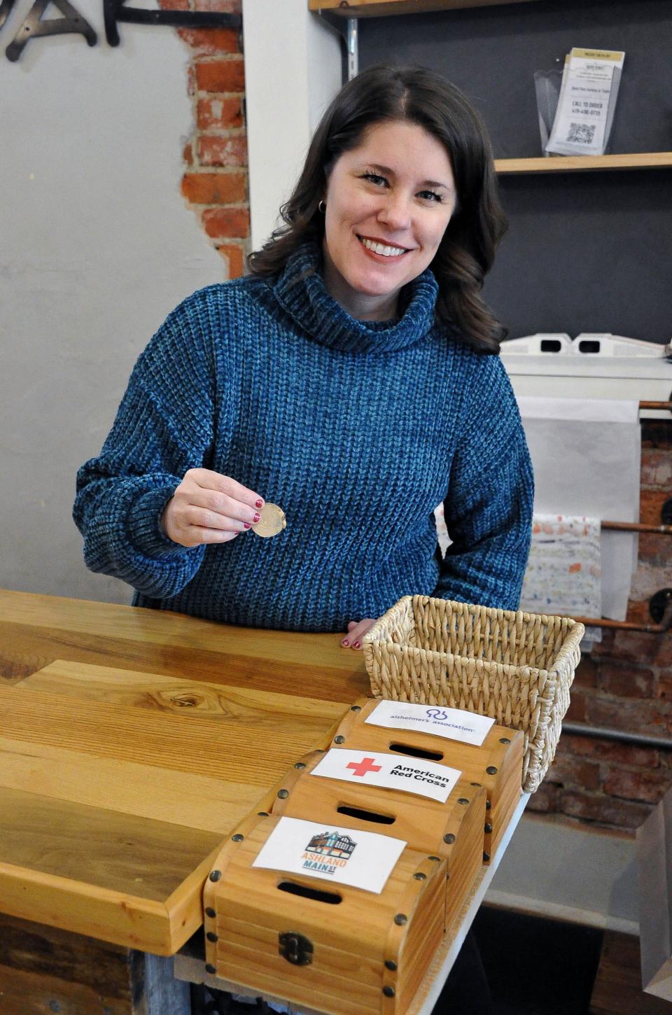 Fig & Oak manager Mary Kettering holds a charity chip that will be dropped by a customer into on one of the three boxes.. A portion of every sale is donated to a local charity of the customers choice.