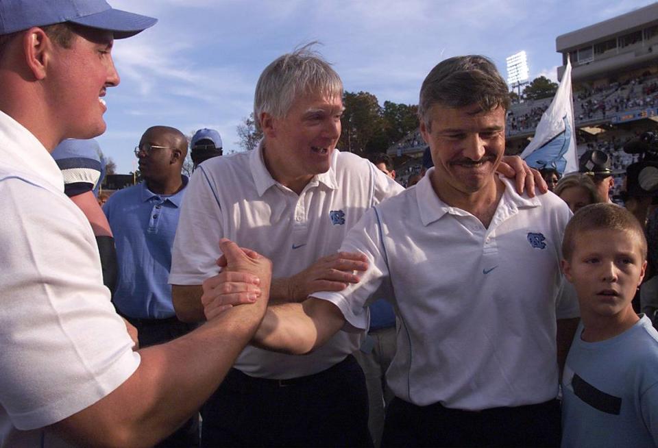 UNC’s Carl Torbush leaves Kenan Stadium with his son Trey as he’s congratulated by assistant coach Kenny Browning after a Tar Heel win in 1999. Chuck Liddy/File photo