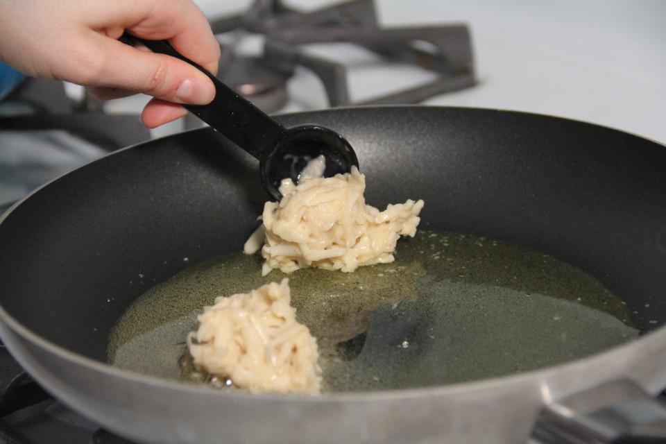 Spooning latke batter into a saucepan for frying.