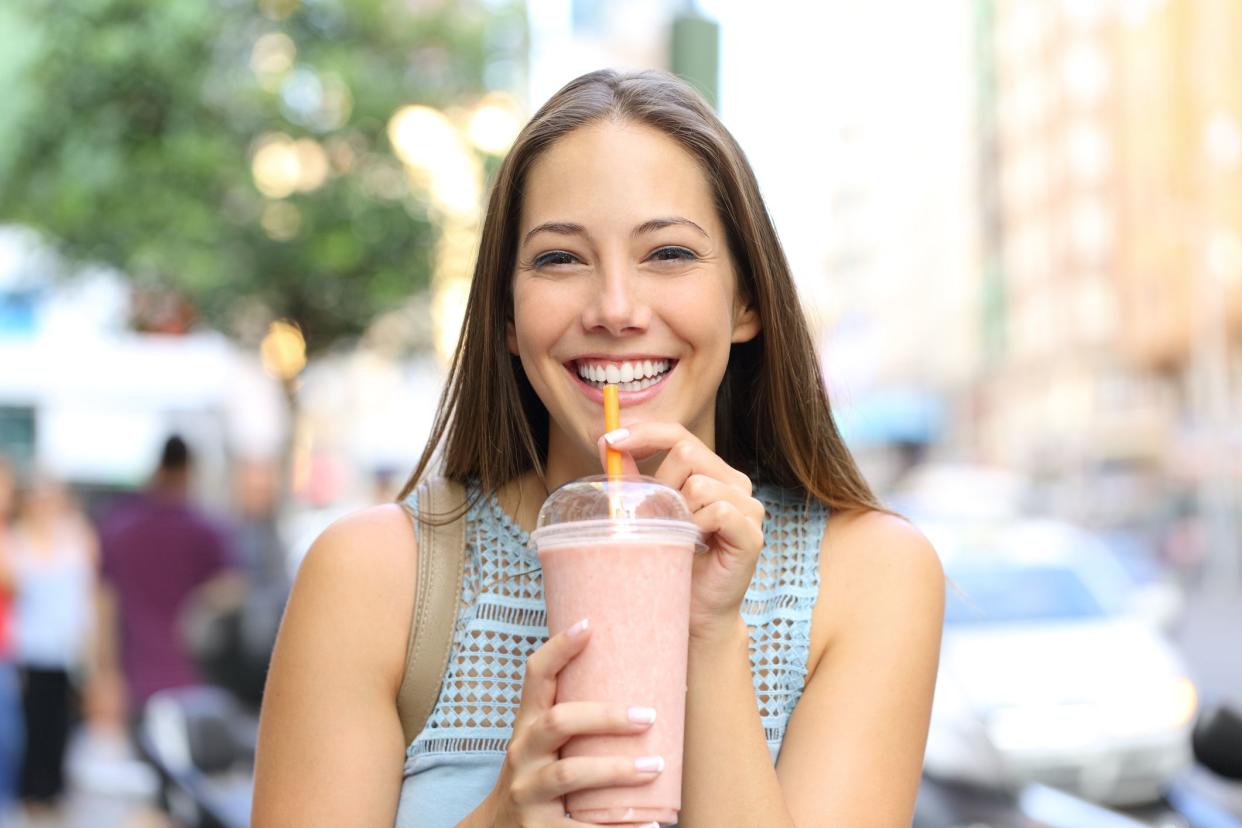 Happy girl looking at you drinking milkshake in the street