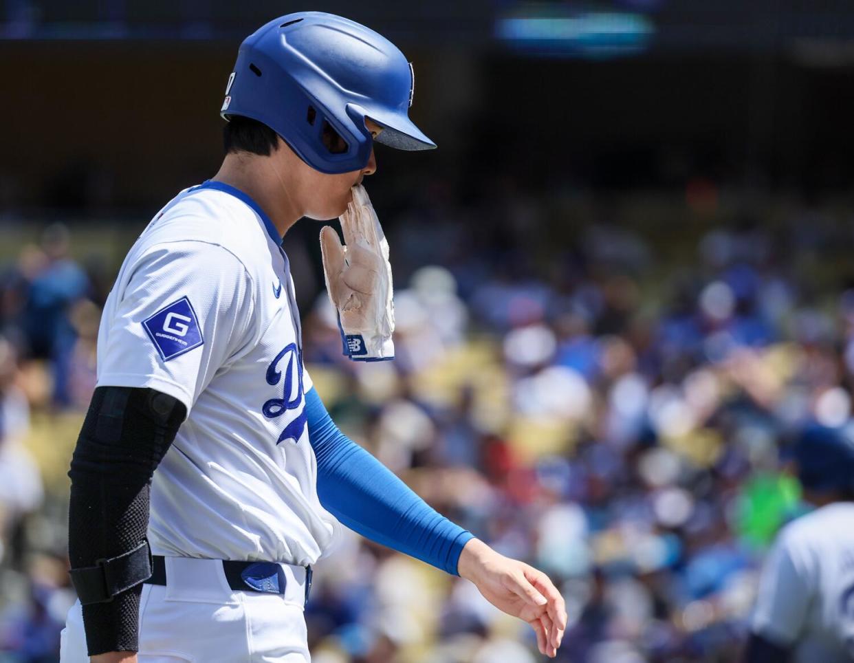 Dodgers' Shohei Ohtani has a battling glove in his mouth as he walks to the dugout during a game against the Nationals