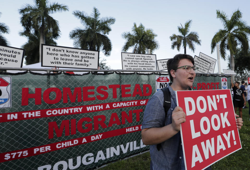 Kody Hersh holds a sign in front of a mock fence representing the Homestead Temporary Shelter for Unaccompanied Children, during a protest against the detention center, outside of the Knight Concert Hall at the Adrienne Arsht Center for the Performing Arts of Miami-Dade County, where a Democratic presidential debate is taking place, Wednesday, June 26, 2019, in Miami. (AP Photo/Lynne Sladky)