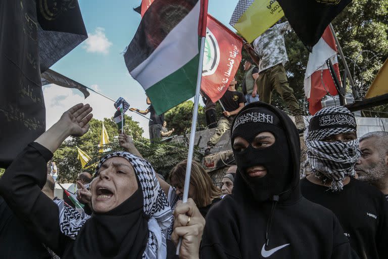 Una mujer palestina entona consignas cerca de dos jóvenes palestinos con capuchas de la Jihad Islámica durante una manifestación en apoyo a la Franja de Gaza en Beirut. 