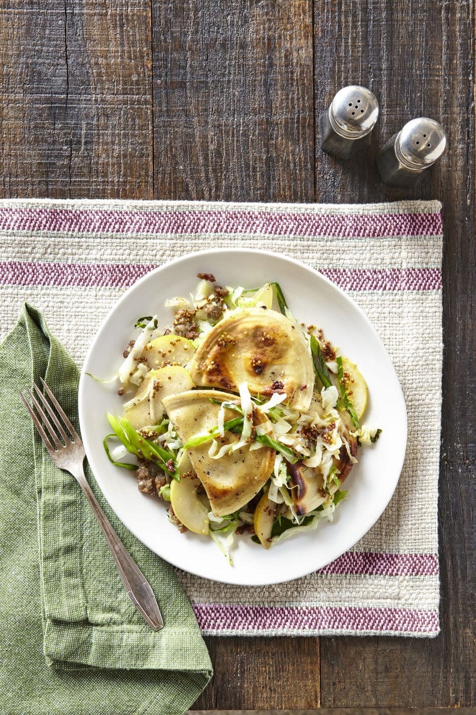 pierogies with sausage cabbage and pear on a white plate with a fork