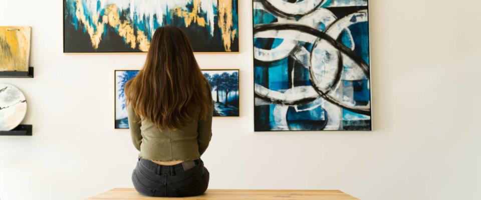 Young female visitor looking reflective while sitting on a bench and admiring the various paintings on the wall of an art gallery