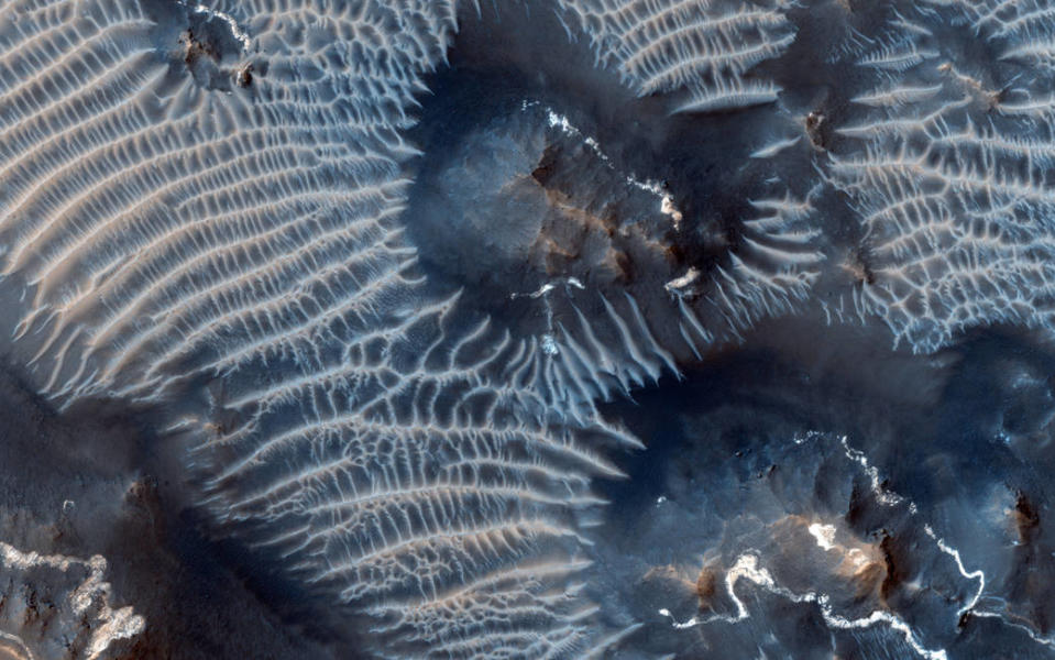 <p>Diese Aufnahme stammt aus der Noctis-Labyrinthus-Region des Planeten, die sich hoch auf dem Valles Marineris befindet. Sie zeigt zwei verschiedene Arten von Sedimenten, die vom Wind verschleppt wurden. Spektakulär sind auch die komplexen Furchengebilde um die Gesteine – von der NASA als “Transverse Aeolian Ridges” bezeichnet. Über diese gibt es bis heute nur wenig Erkenntnisse. (Bild: NASA/JPL-Caltech/Univ. of Arizona) </p>