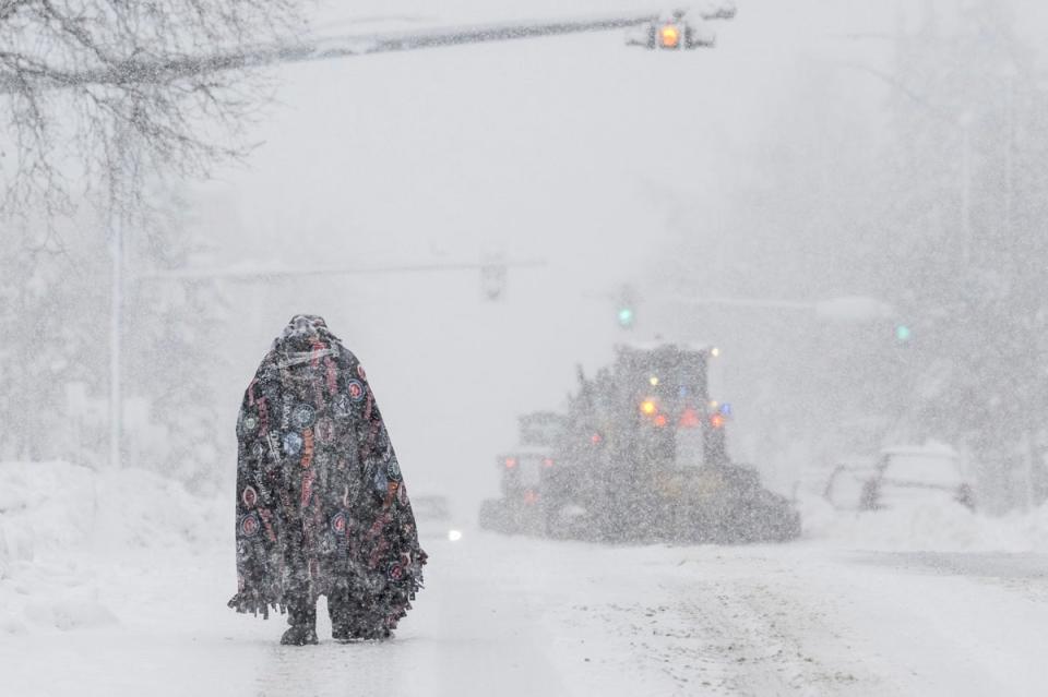 A pedestrian takes cover under a blanket in Anchorage as plows clear the roadway on 9 November (Anchorage Daily News)