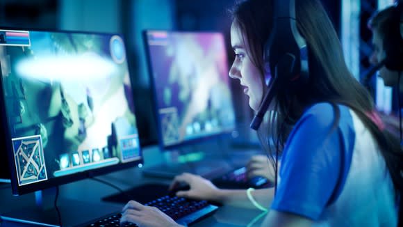 A young woman sitting at a computer, wearing a headset and playing a video game.