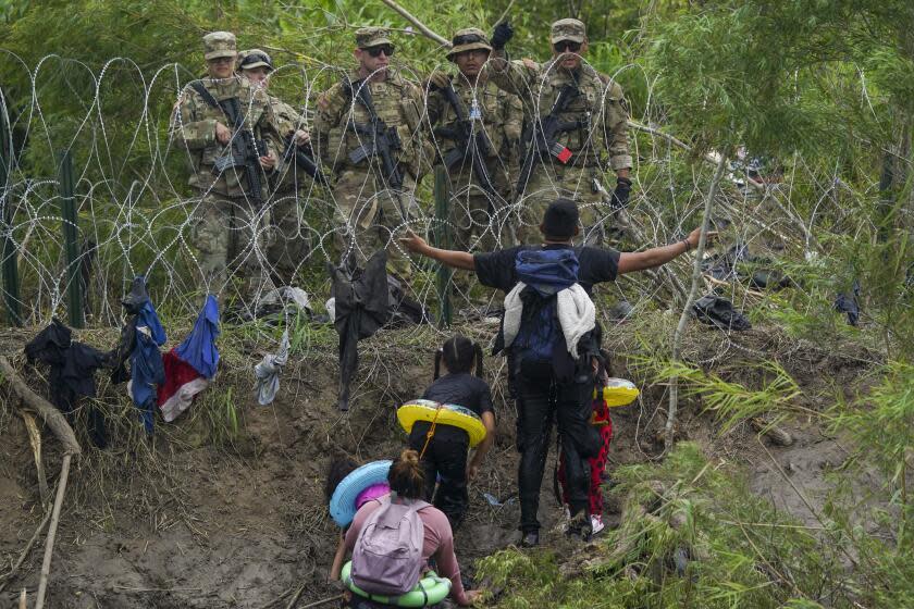 Un migrante abre los brazos frente a miembros de la Guardia Nacional de Texas ubicados detrás de alambre de púas en una de las márgenes del río Bravo, el jueves 11 de mayo de 2023, vistos desde Matamoros, México. (AP Foto/Fernando Llano)