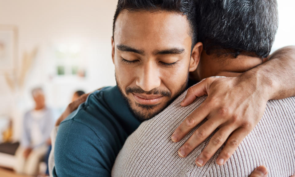 Two men embracing in a comforting hug, with others in the background