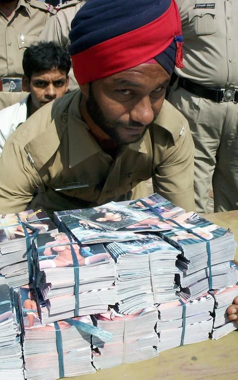 An Indian police officer handles pornographic magazines seized during a raid in Patiala - Credit: Getty Images/AFP