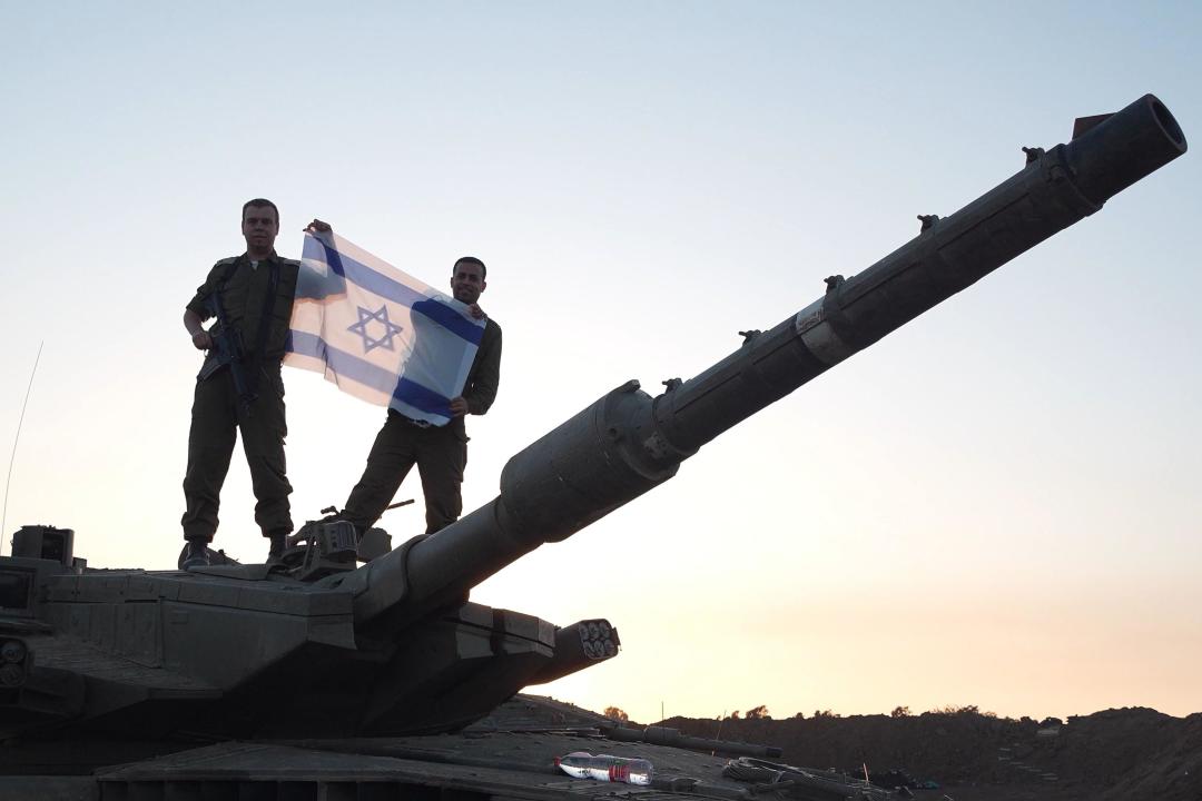Israeli soldiers hold an Israeli flag as they stand on a tank deployed near the border with Gaza strip after returning from Gaza on the sixth day of a truce between Israel and Hamas on November 28, 2023 in Be'eri, Israel. Israel and Hamas agreed to a two-day extension to their initial four-day truce, which promised the release of more Israeli hostages held in Gaza, as well as the release of Palestinian prisoners held in Israeli jails.