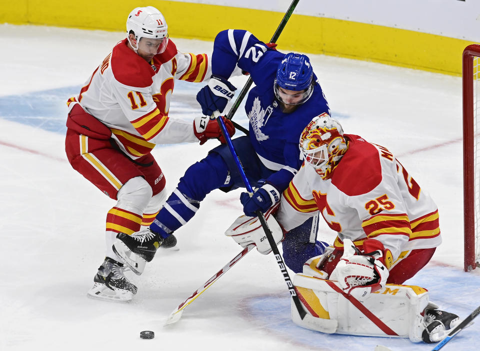 Calgary Flames goaltender Jacob Markstrom (25) makes a save as Flames' Mikael Backlund (11) and Toronto Maple Leafs' Alex Galchenyuk (12) look for a rebound during the second period of an NHL hockey game Tuesday, April 13, 2021 in Toronto. (Frank Gunn/Canadian Press via AP)