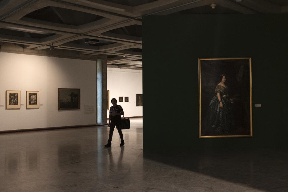 In this Sept. 17, 2019, photo, a woman walks between European paintings in the dark in the Museum of Fine Arts of Caracas, Venezuela. Only about a third of the 18 galleries are open to the public; the rest have been closed for months due to renovations, although there’s no sign any are taking place. (AP Photo/Andrea Hernandez Briceño)