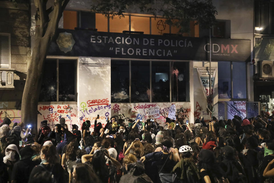 FILE - In this Aug. 16, 2019 file photo, female demonstrators stand outside a defaced police station as they watch the second floor burn, from a fire they started, during a protest sparked by a string of alleged sexual attacks by police officers, in Mexico City. Tired of impunity for rapists and murderers, dozens of women trashed a bus station, defaced the Angel of Independence monument with spray paint and set a police station ablaze during the August protest in the capital. The vandalism prompted widespread discussion about how best to draw attention to what many agree is a pressing issue for the country. (AP Photo/Emilio Espejel, File)