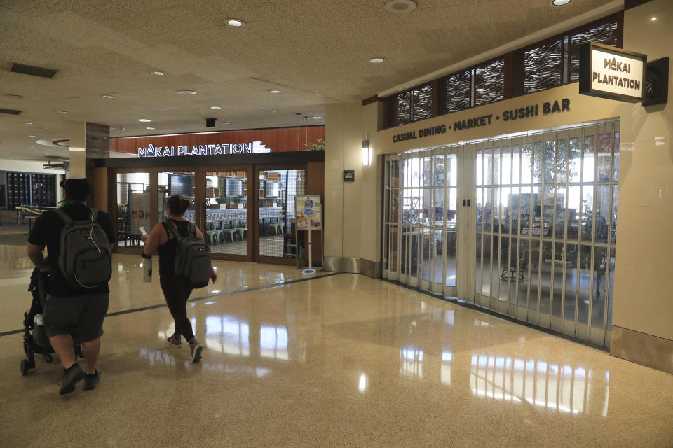 Vistors walk past closed shops inside the Daniel K. Inouye International Airport Thursday, Oct. 15, 2020, in Honolulu. The COVID-19 pandemic has caused a devastating downturn on Hawaii's tourism-based economy. Many stores and restaurants inside the airport remain close due the the economic crisis. (AP Photo/Marco Garcia)