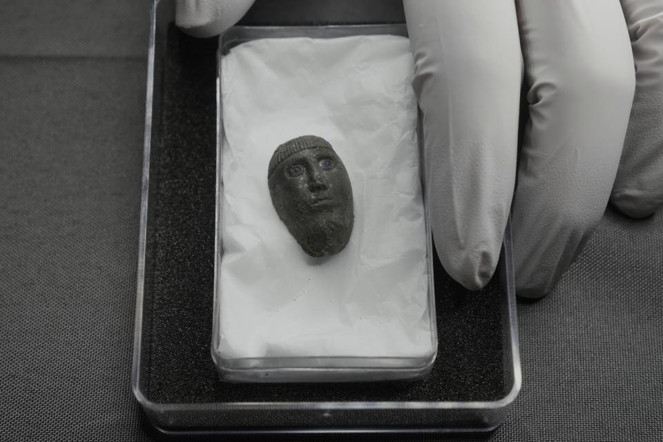 Liz Barham, senior conservator of the Museum of London Archaeology, displays an early medieval silver head with blue glass eyes during a photo call, in London, Tuesday, Dec. 6, 2022. A silver head found during construction of a housing development marks the grave of a powerful woman who may have been an Anglo-Saxon aristocrat or early Christian religious leader in Britain. (AP Photo/Kin Cheung)