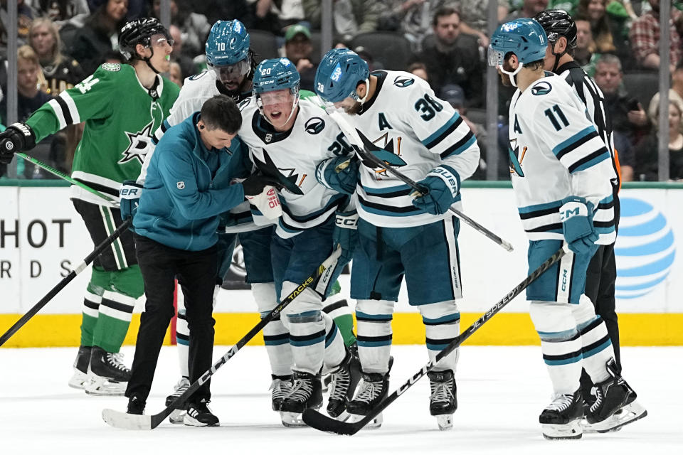 San Jose Sharks left wing Fabian Zetterlund (20) is assisted off the ice by a team staff member, Anthony Duclair (10) and Mario Ferraro (38) during the second period of the team's NHL hockey game against the Dallas Stars in Dallas, Saturday, March 2, 2024. (AP Photo/Tony Gutierrez)