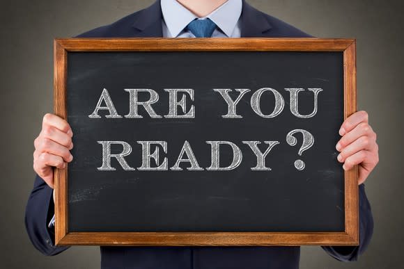 man in suit holding small chalkboard on which is printed are you ready?