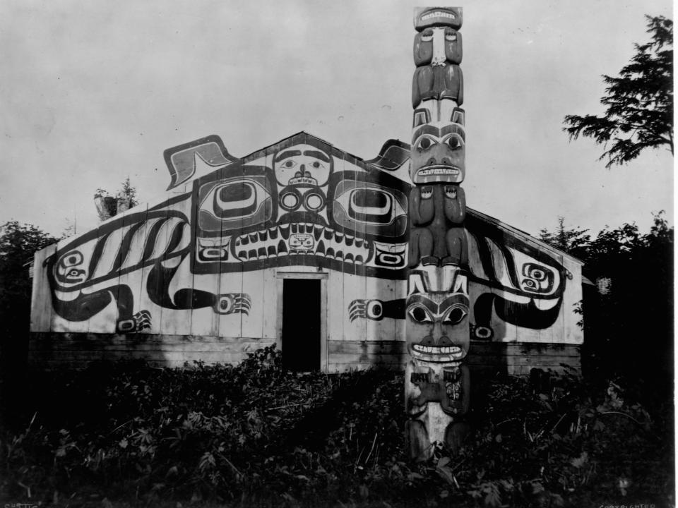 A totem pole guards the entrance to an eloborately decorated Northwest Indian Lodge House, Alaska, 1899.