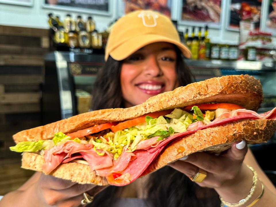 A photo of Erica Noblecilla in a restaurant holding a large sandwich