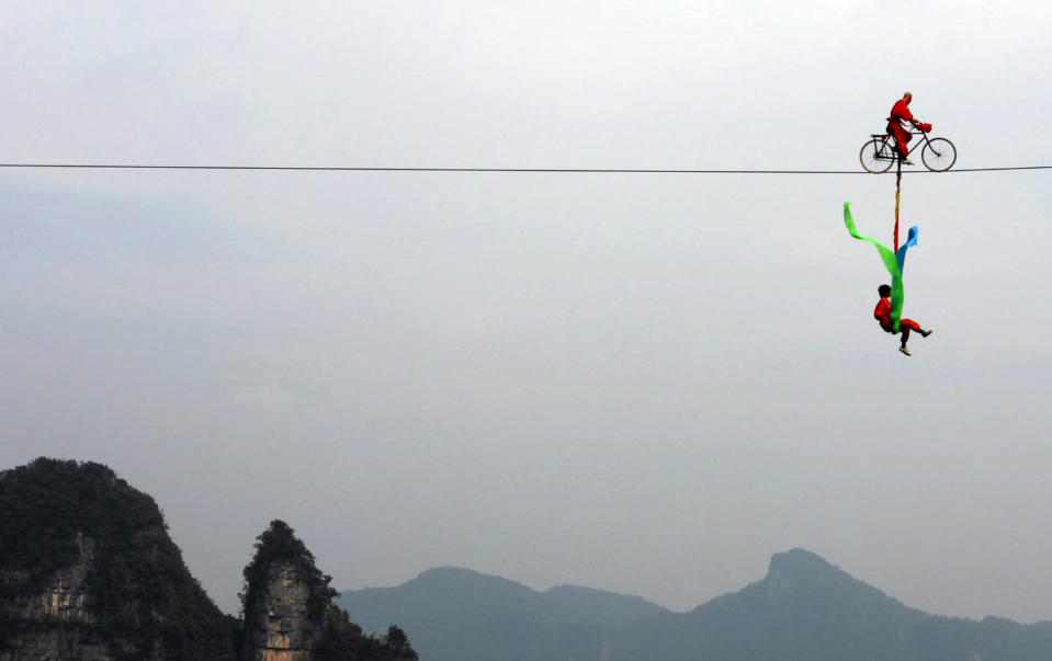 Acrobats ride a bicycle during a stunt performance 1000 meters (3300 feet) above the ground at Chaibuxi National Forest Park in Wufeng Tujia minority autonomous county, in central China's Hubei province, October 9, 2006. Picture taken October 9, 2006. CHINA OUT REUTERS/China Daily