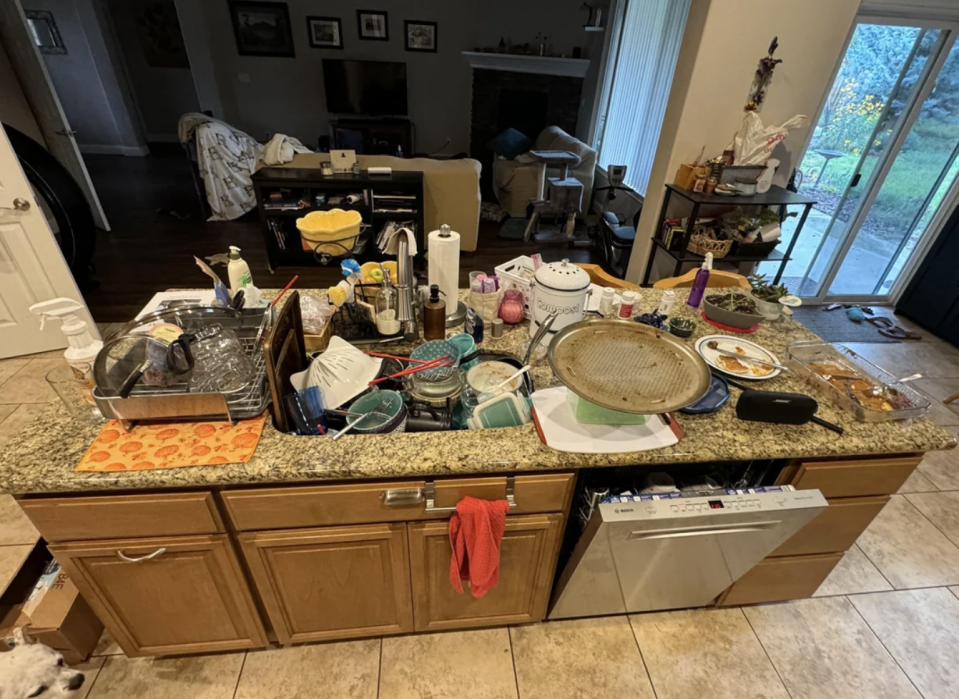 A cluttered kitchen counter with dishes, food containers, and various items spread out.