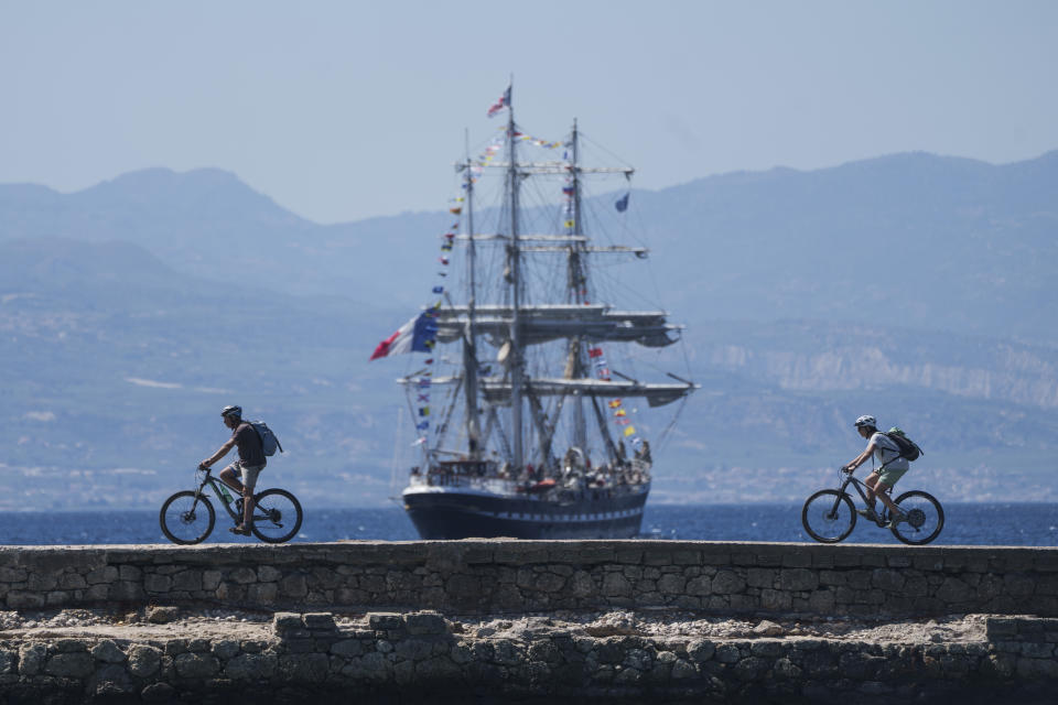 FILE - Cyclists pass in front of the Belem, the three-masted sailing ship carrying the Olympic flame to France, as it sails near Corinth, Greece, April 28, 2024. The Olympic torch finally enters France when it reaches the southern seaport of Marseille on Wednesday May 8, 2024, on an armada from Greece. After leaving Marseille a vast relay route will be undertaken before the torch's odyssey ends on July 27 in Paris. (AP Photo/Petros Giannakouris, File)