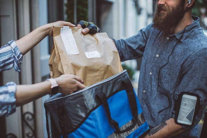 Delivery person in casual attire handing over a paper bag to a customer at a doorstep