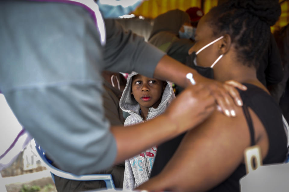 A Kenyan woman receives a dose of AstraZeneca coronavirus vaccine donated by Britain, as her son watches, at the Makongeni Estate in Nairobi, Kenya Saturday, Aug. 14, 2021. In late June, the international system for sharing coronavirus vaccines sent about 530,000 doses to Britain – more than double the amount sent that month to the entire continent of Africa. It was the latest example of how a system that was supposed to guarantee low and middle-income countries vaccines is failing, leaving them at the mercy of haphazard donations from rich countries. (AP Photo/Brian Inganga)