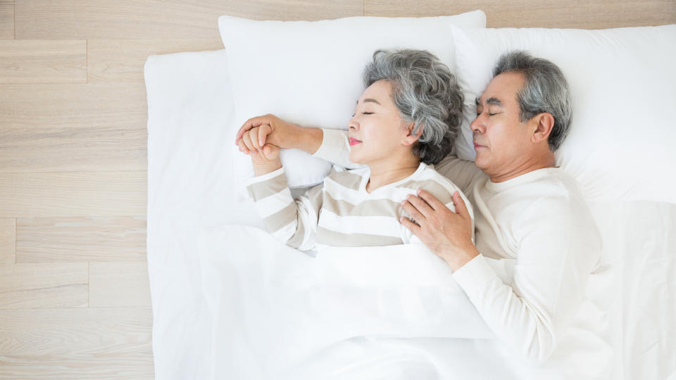 A senior couple cuddle while sleeping in a white bed