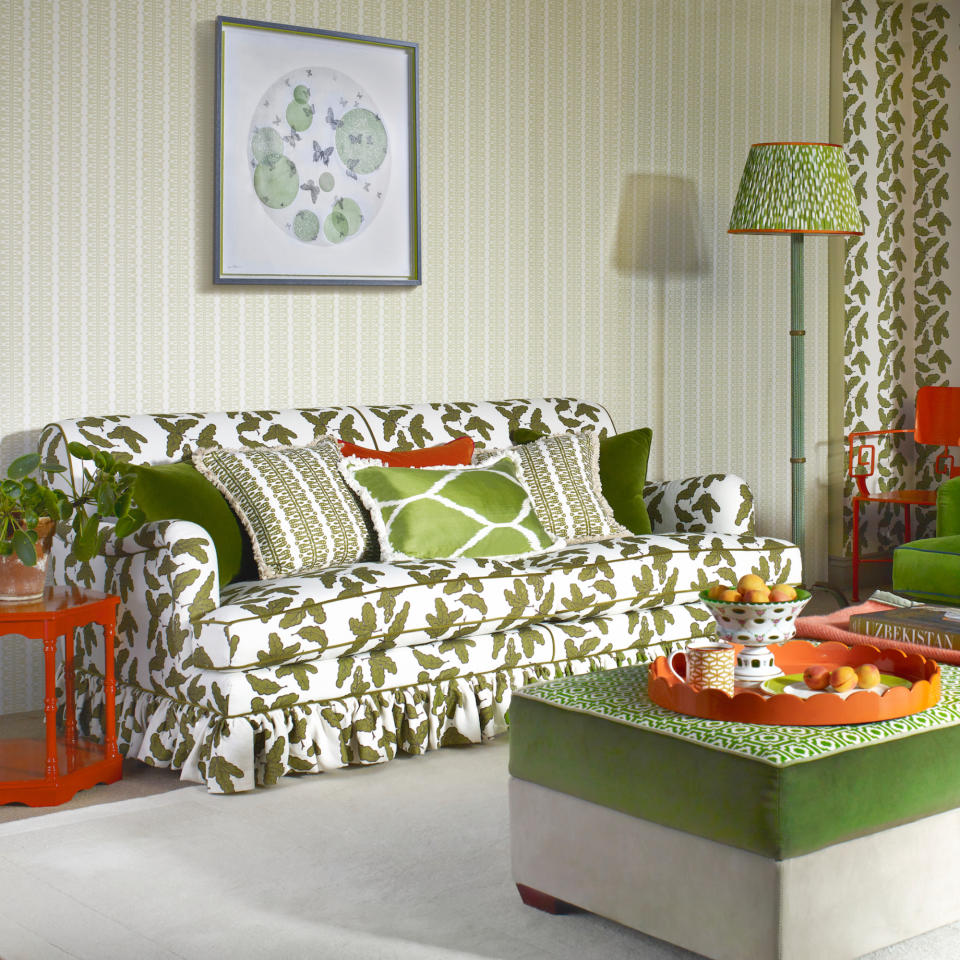 green living room with upholstered sofa, green and cream footstool, subtle green wallpaper, artwork, cushions, floor lamp with green patterned lampshade