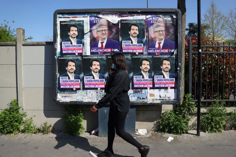 A young woman walks past an official campaign poster of French far-left leader Jean-Luc Melenchon in Aubervilliers
