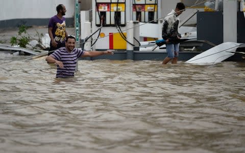People walk next to a gas station flooded and damaged by the impact of Hurricane Maria - Credit: AP