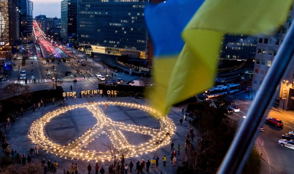 People stand around a giant peace sign with the message 'Stop Putin's Oil', put up by demonstrators ahead of an EU and NATO summit in Brussels (AP)