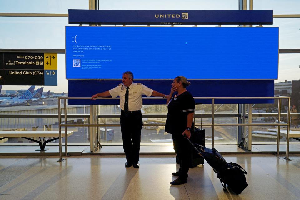 United Airlines employees wait by a departures monitor displaying a blue error screen, also known as the “Blue Screen of Death” inside Terminal C in Newark International Airport, after United Airlines and other airlines grounded flights due to a worldwide tech outage caused by an update to CrowdStrike's "Falcon Sensor" software.