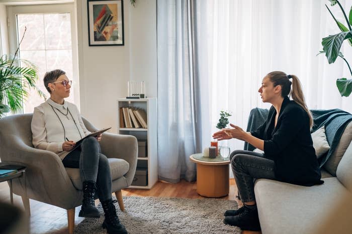 Two individuals having a conversation, one taking notes, in a cozy room with plants