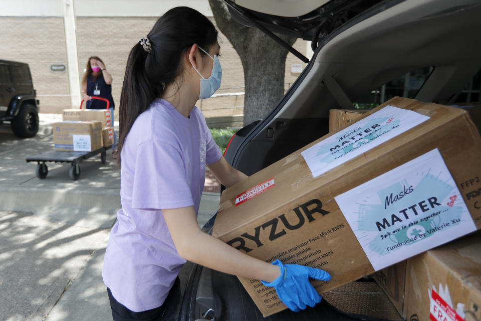 Valerie Xu, 15, carries boxes of mask to a waiting cart held by UT Southwestern Medical Center employee, Cindy Levy, in Dallas, Friday, June 5, 2020. Xu raised the funds to buy the mask and make the donation to the hospital. (AP Photo/Tony Gutierrez)
