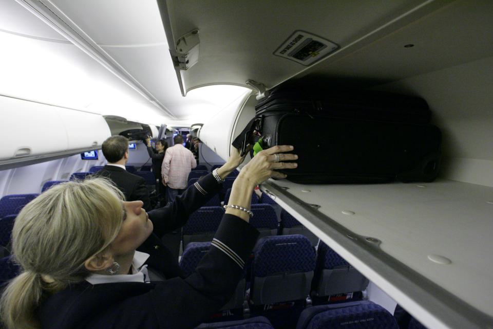 Stock photo of flight attendant placing items in an overhead bin. Source: AP