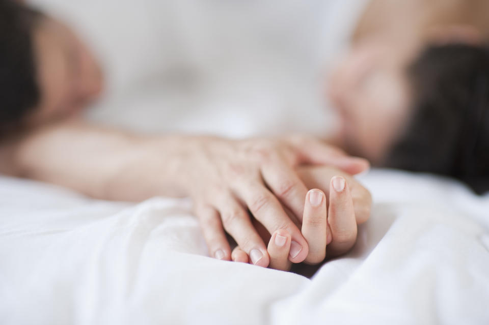 A close-up of a couple lying in bed, holding hands, with their faces blurred in the background