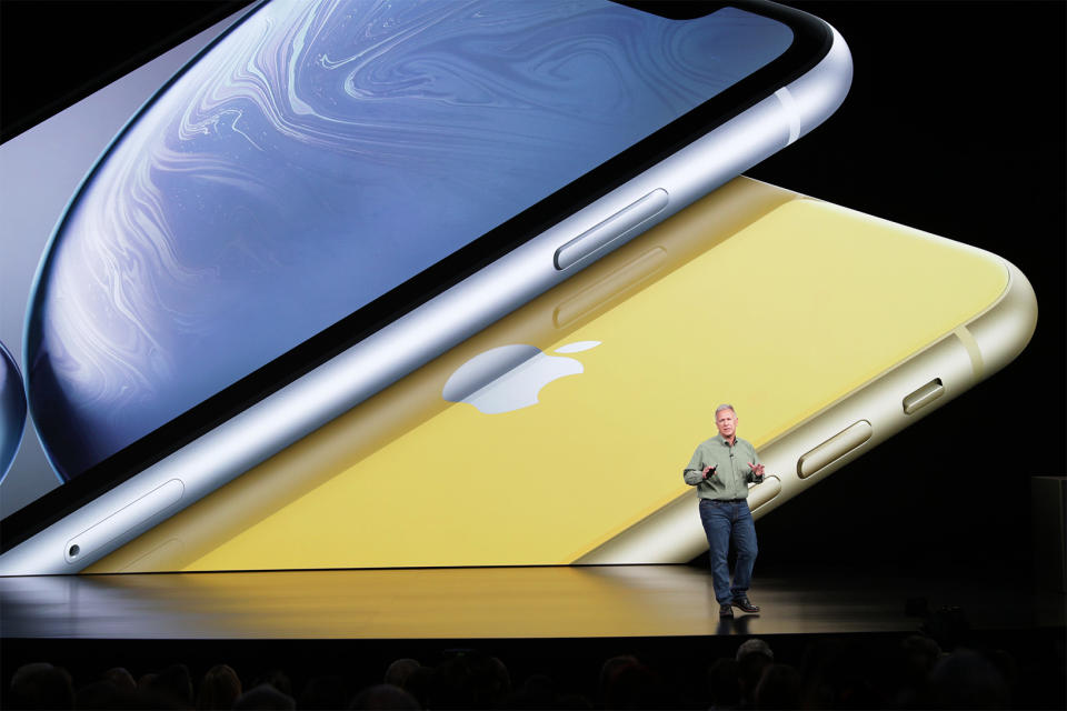 Apple executive Phil Schiller onstage, in front of a giant image of a blue iPhone XR stacked on a yellow one