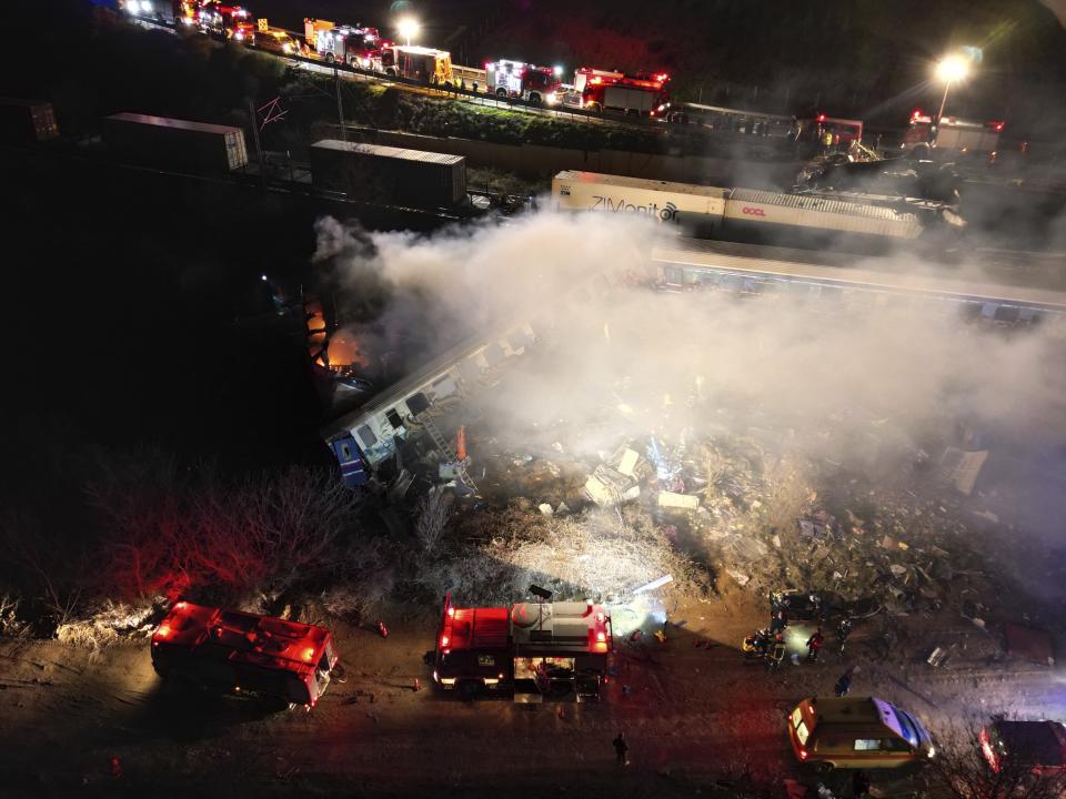 Smoke rises from trains as firefighters and rescuers operate after a collision near Larissa city, Greece, early Wednesday, March 1, 2023. The collision between a freight and passenger train occurred near Tempe, some 380 kilometers (235 miles) north of Athens, and resulted in the derailment of several train cars. (AP Photo/Vaggelis Kousioras)