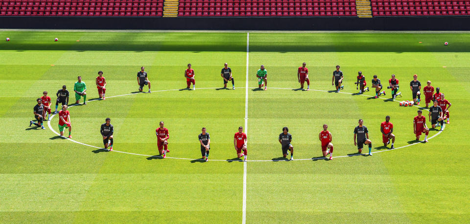 Jugadores del Liverpool arrodillados en torno al círculo central del terreno de juego durante un entrenamiento en Anfield