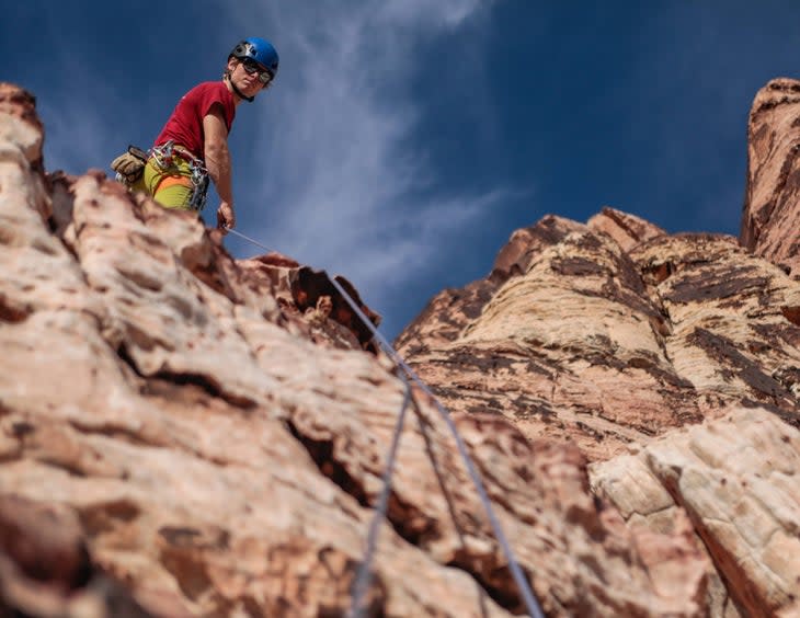 Cody Bradford belays climber from atop a cliff.