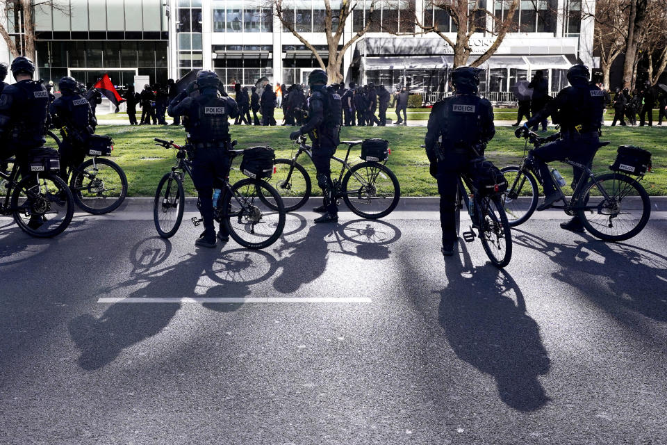Bicycle-mounted Sacramento Police Officers watch as black clad protesters march through downtown Sacramento, Calif, Wednesday, Jan. 20, 2021. The protesters had made their way to the Capitol where they were stopped by the 6-foot high chain-link fence installed to stop violence on the Inauguration Day of President Joe Biden and Vice President Kamala Harris. (AP Photo/Rich Pedroncelli)