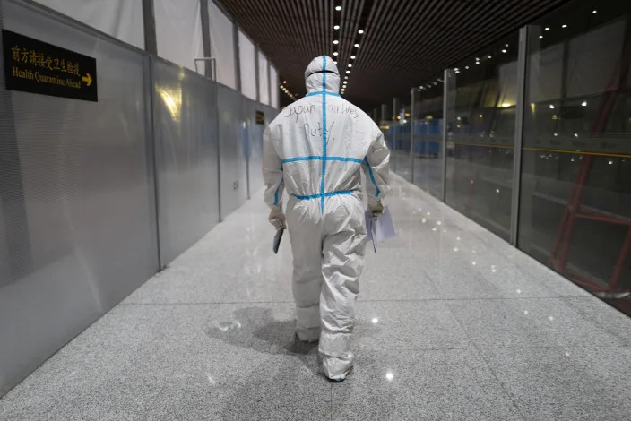 FILE - A member of airport personnel dressed in protective gear leads passengers into the customs area at the Beijing Capital International Airport ahead of the 2022 Winter Olympics in Beijing, Jan. 24, 2022. (AP Photo/Jae C. Hong, File)
