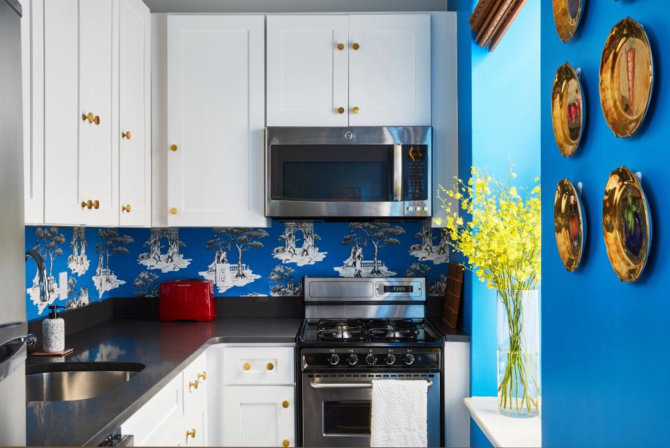 Brass hardware and white cabinetry are paired with a bright blue wallpaper. The white space allows the printed backsplash to shine.