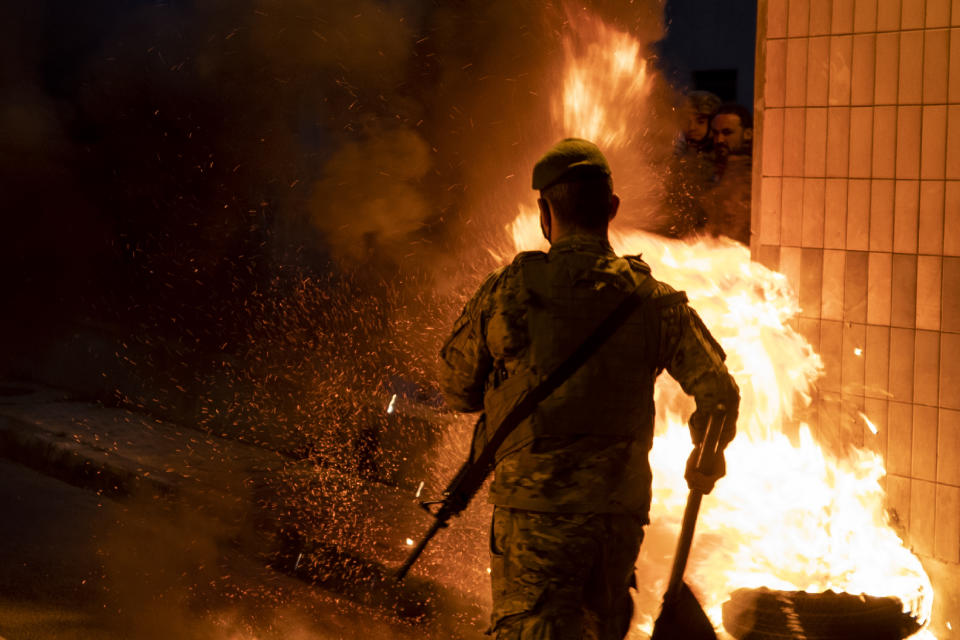 A Lebanese soldier removes burning tires placed by supporters of Prime Minister-designate Saad Hariri to block a road link to Beirut international airport in Beirut, Lebanon, Monday, March 22, 2021. Protesters blocked some roads in the Lebanese capital with burning tires Monday after talks on the formation of a new Cabinet broke down, heralding more economic and financial collapse for the small Arab country. (AP Photo/Hassan Ammar)