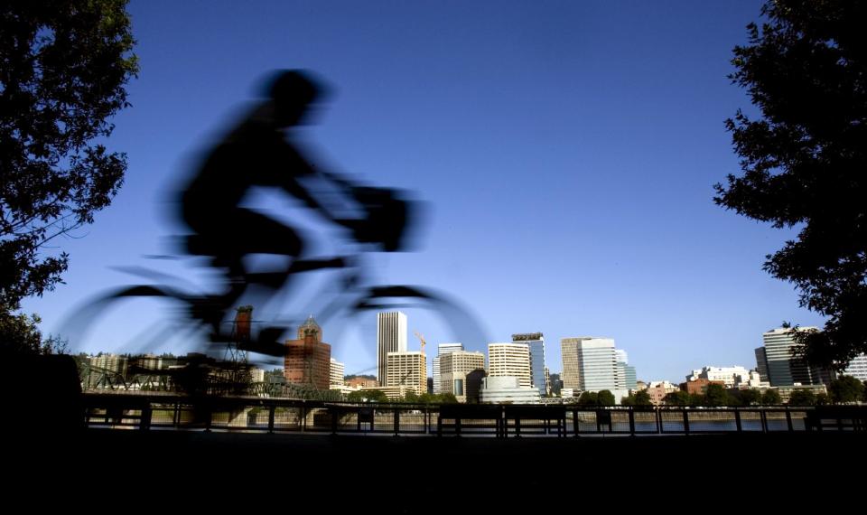 FILE-  In this July 10, 2008 file photo, a bicyclist is a blur traveling along the east bank of the Willamette River as the downtown skyline is bathed in early morning sunlight in Portland, Ore. Researchers at Portland State University found that the Portland atmosphere and culture is a magnet for the young and college educated, even though a disproportionate share of them are working in part-time jobs or positions that don’t require a college degree. (AP Photo/Don Ryan, File)